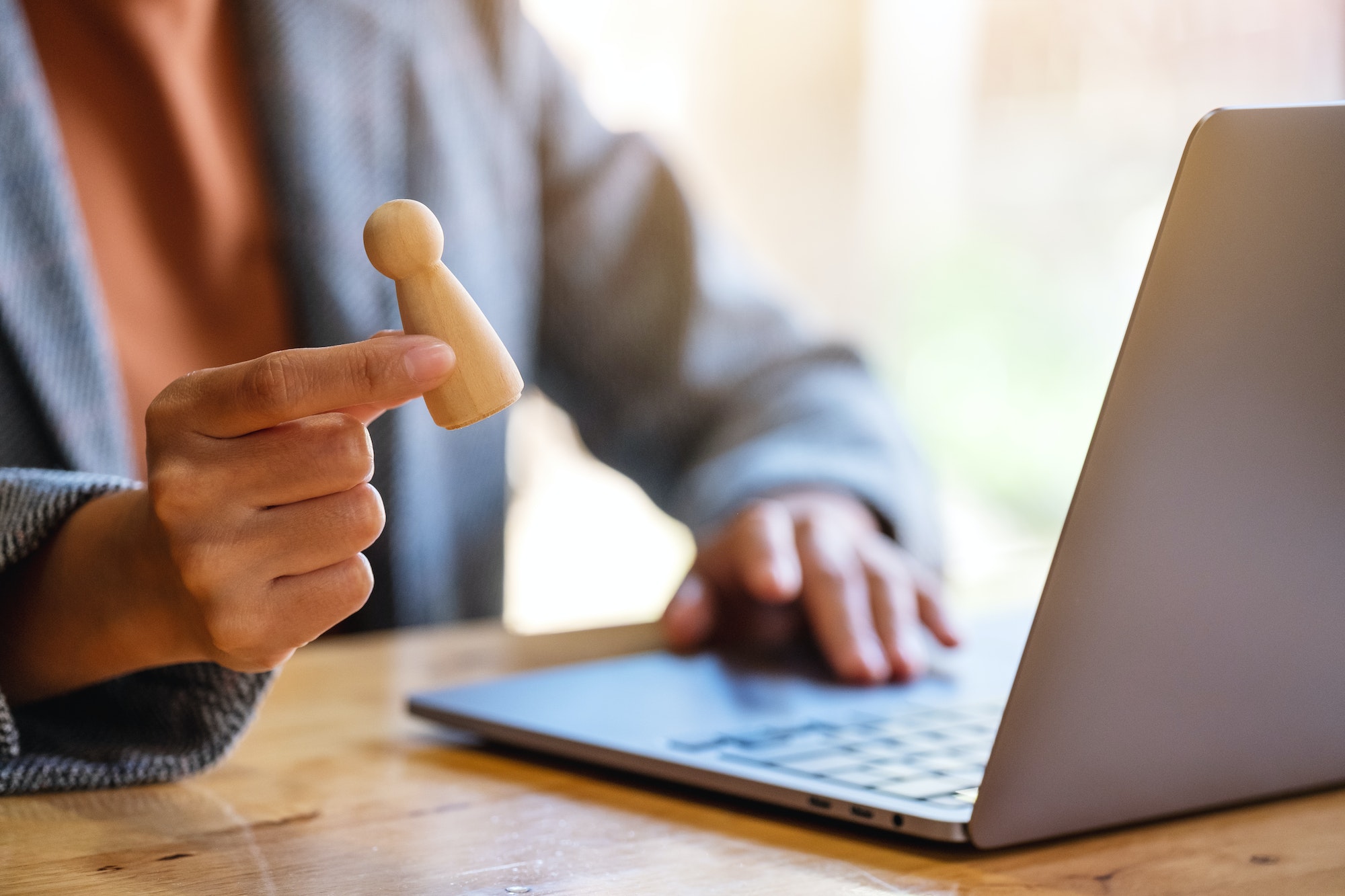 Businesswoman leader holding and choosing wooden people while working on laptop computer in office